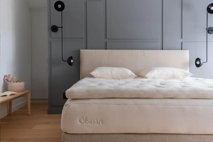 Minimalist Scandinavian bedroom with an Obasan mattress, gray paneled walls, and light wood flooring.