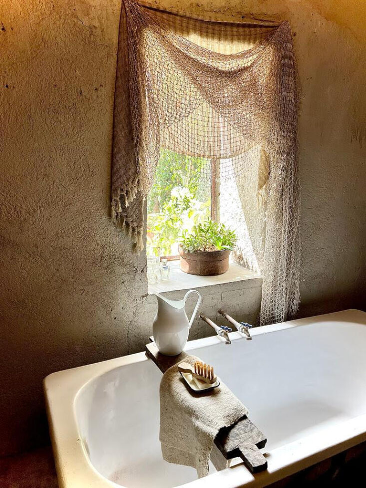 Rustic bathroom featuring a recycled tub, copper piping, and fishing net curtains.