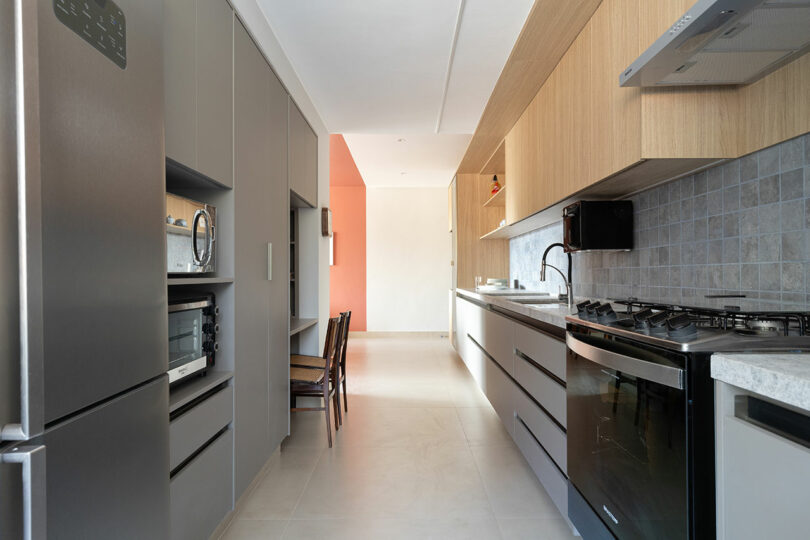 A modern galley kitchen with a clear linear path, light flooring, and a bright accent wall at the end of the corridor.
