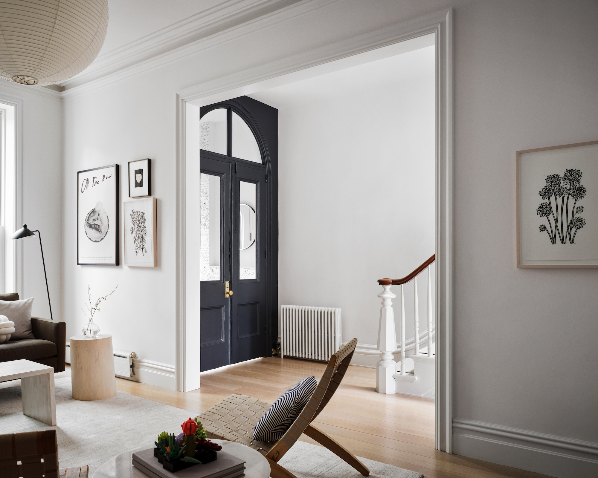 Modern minimalist living room with light wood floors, a black arched door, and paper pendant lamp.