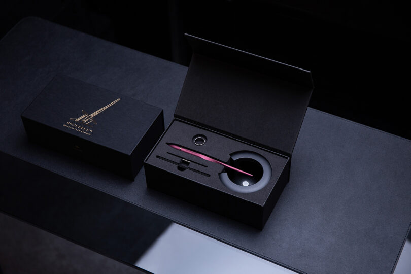 An open luxury presentation box containing a red Novium Hoverpen fountain pen and an ink bottle.