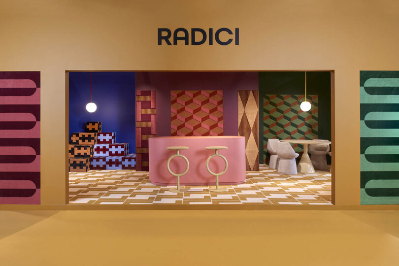 Modern interior with 'RADICI' text and vibrant pink and yellow geometric furniture and walls.