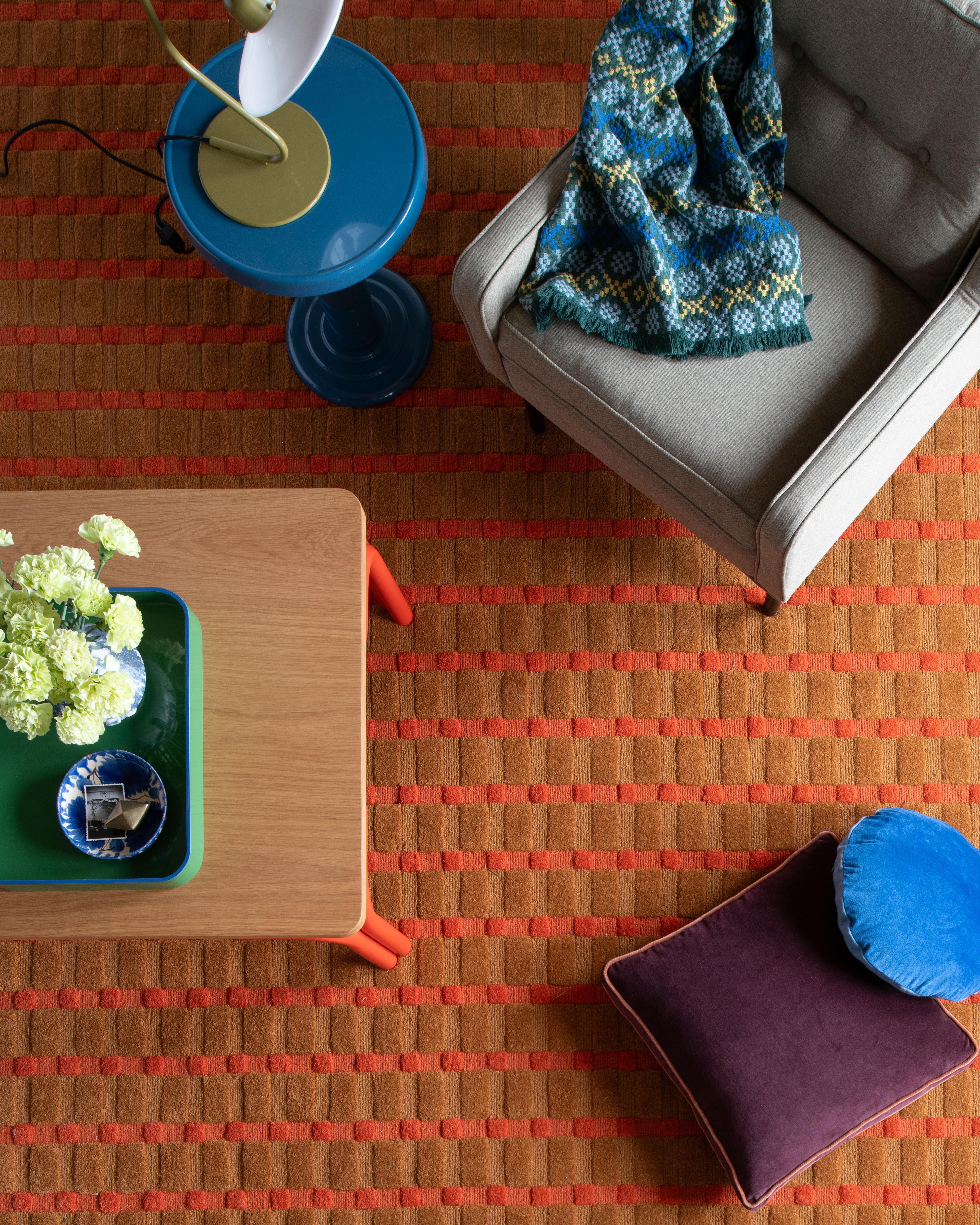 Overhead view of a living room featuring a wooden stool, a textured rug, and two cozy blankets.