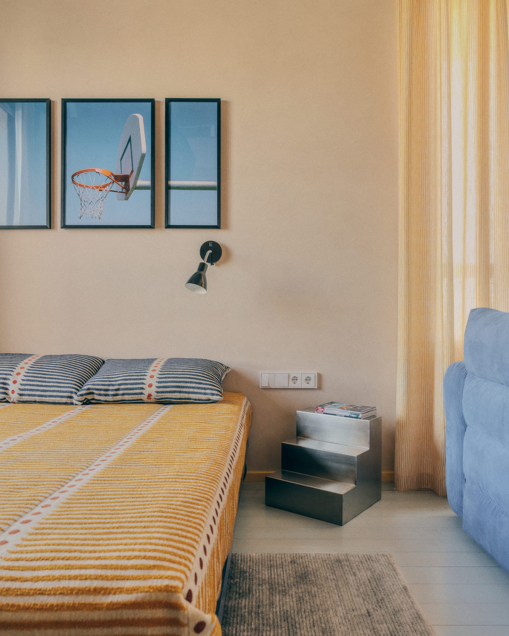 A modern minimalist bedroom with yellow striped bedding, wall-mounted basketball photography, and a metal nightstand.