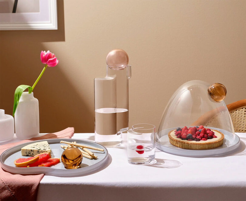 A modern table setting with a pink tart under a glass dome and elegant glassware.