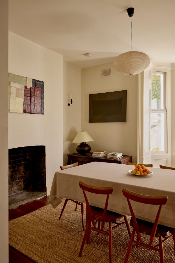 Neutral-toned dining area with mid-century modern wooden chairs and a brick fireplace.