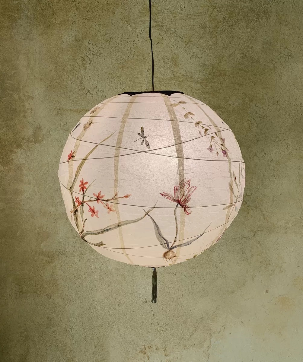 A traditional paper globe lantern with floral and dragonfly motifs against a textured wall.