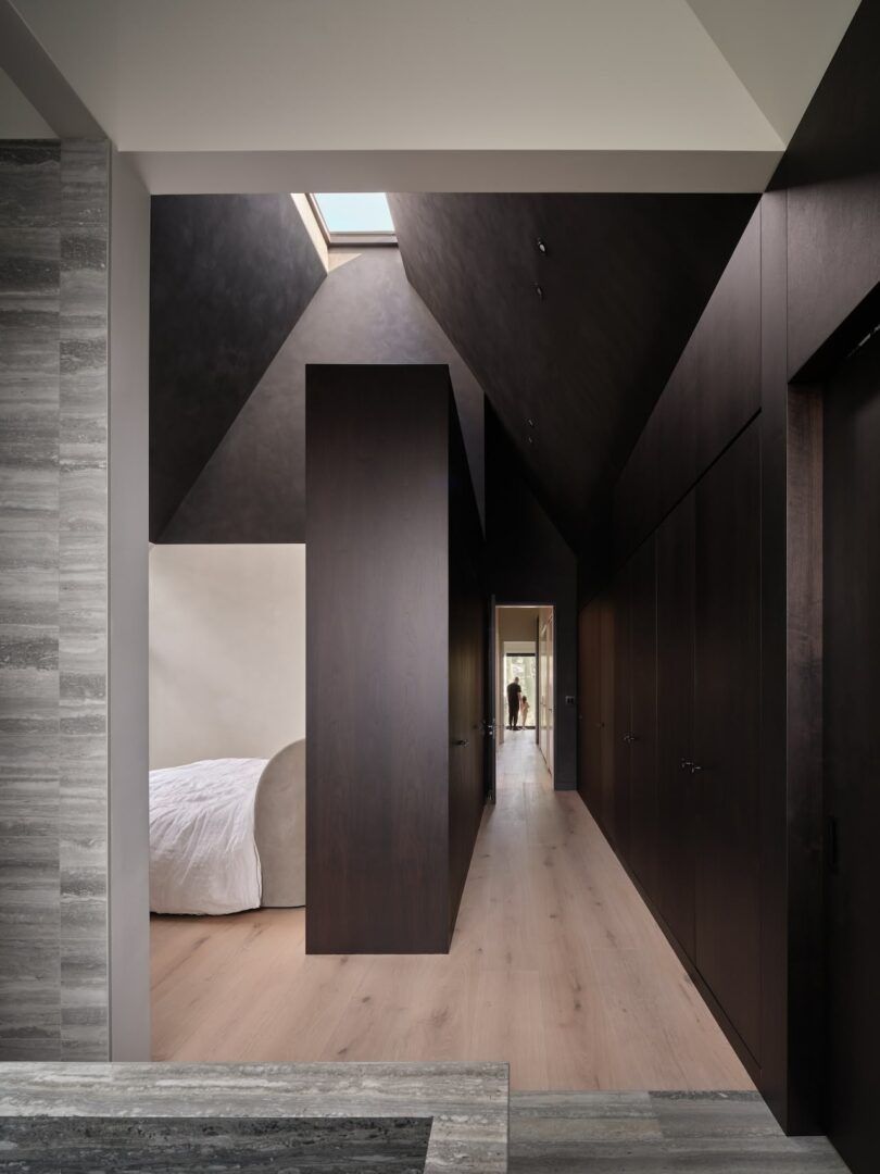 A modern attic bedroom featuring high ceilings, dark wood accents, and a large skylight providing natural light.