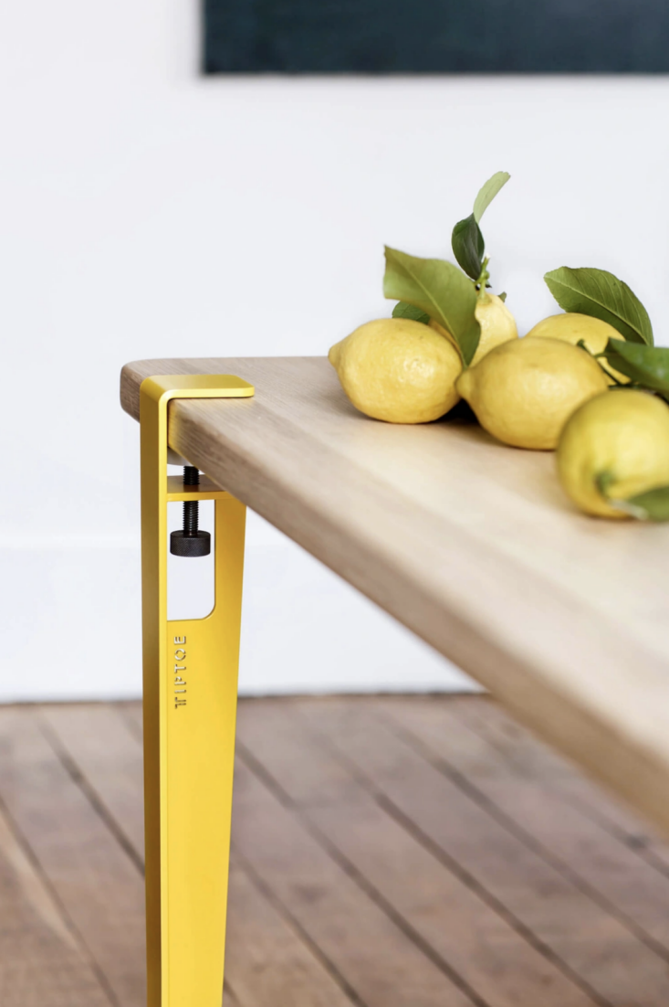 Close-up of a bright yellow Tiptoe clamp-style leg attached to a wooden tabletop.