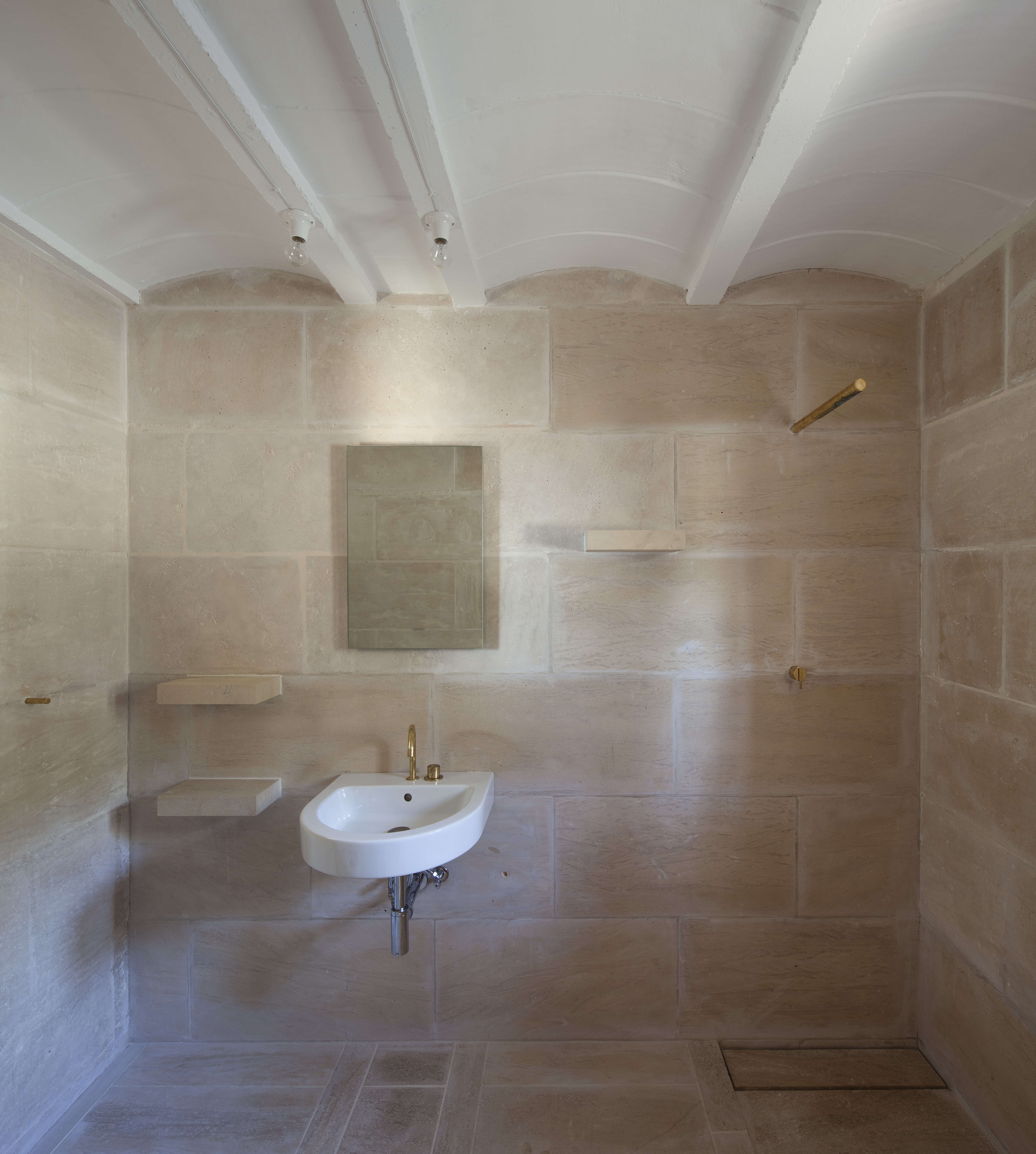 Bathroom with organic stone textures, built-in shelving, and a warm beige color palette.