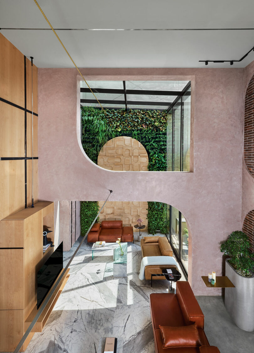 A double-height living room with pink lime plaster walls, arched openings, and expansive windows.