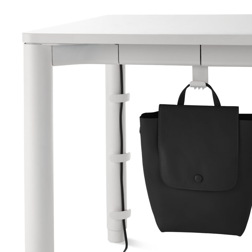 A white desk leg featuring a minimalist black bag hook and cable organizer.