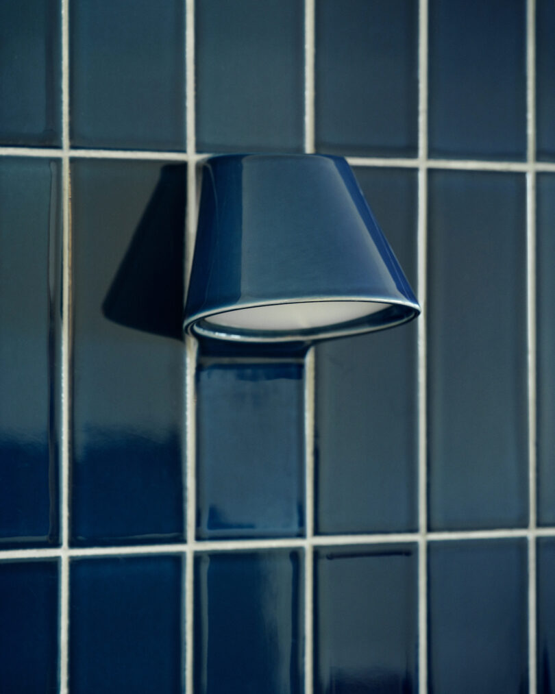 A blue ceramic wall sconce mounted on a matching grid of glossy dark blue tiles.