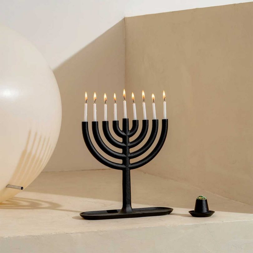 A black cast iron menorah candelabra with a sleek geometric base and lit candles.