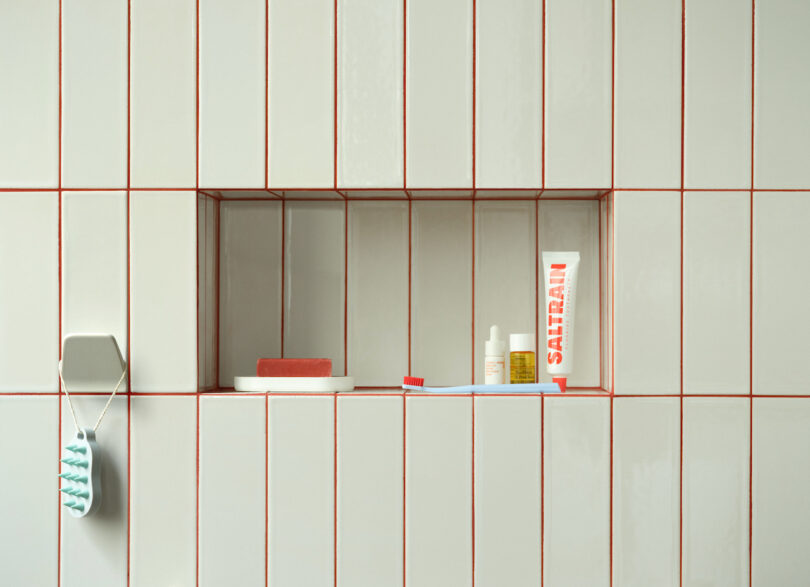 A bathroom niche within a red tiled wall holding soap, toiletries, and a toothbrush hanging from a hook.