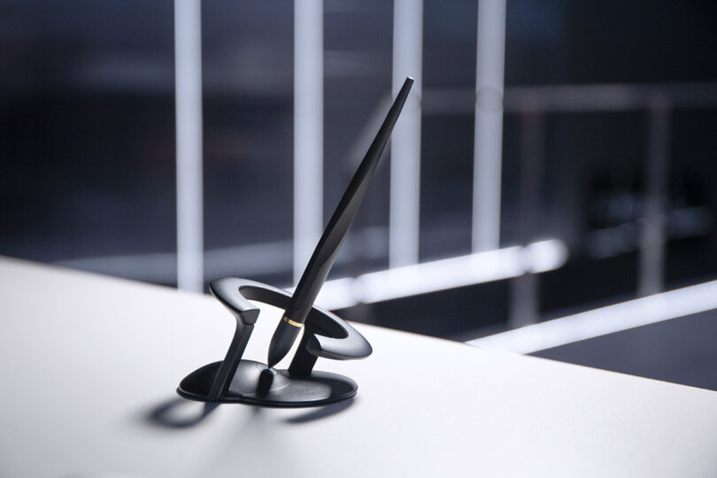 A modern black Novium Hoverpen standing perfectly upright in its magnetic holder on a white surface.