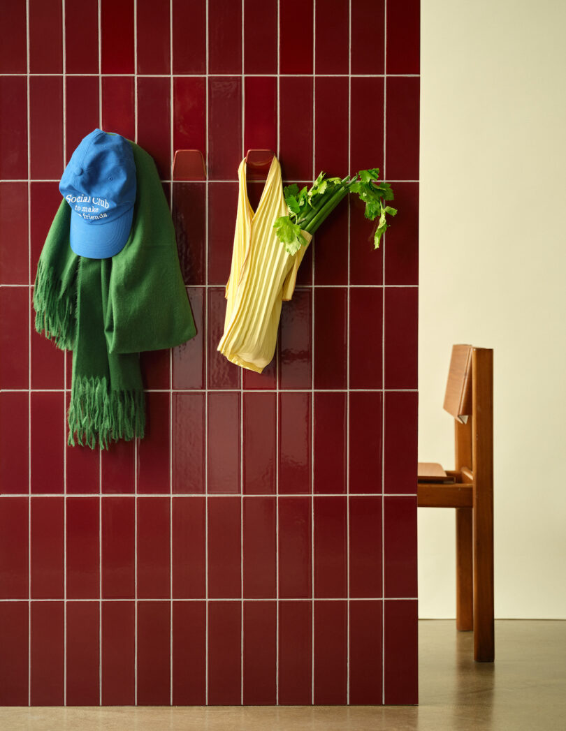 A red tiled wall with ceramic hooks holding a blue hat, yellow bag, and other colorful items.