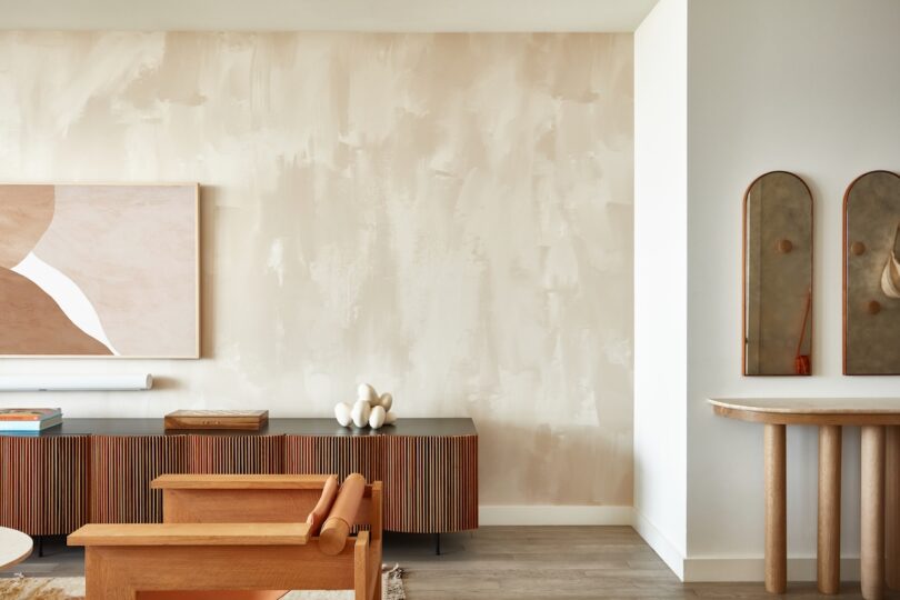 A living room view showing beige textured walls, a wooden sideboard, and abstract art that creates a warm, cocoon-like atmosphere.