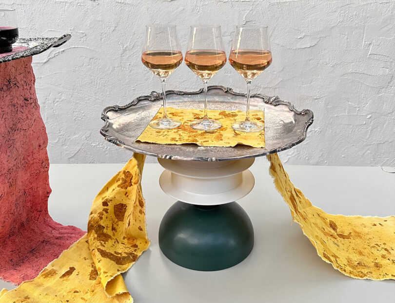Three glasses of wine on a silver tray with yellow textured paper and a green-and-white pedestal.