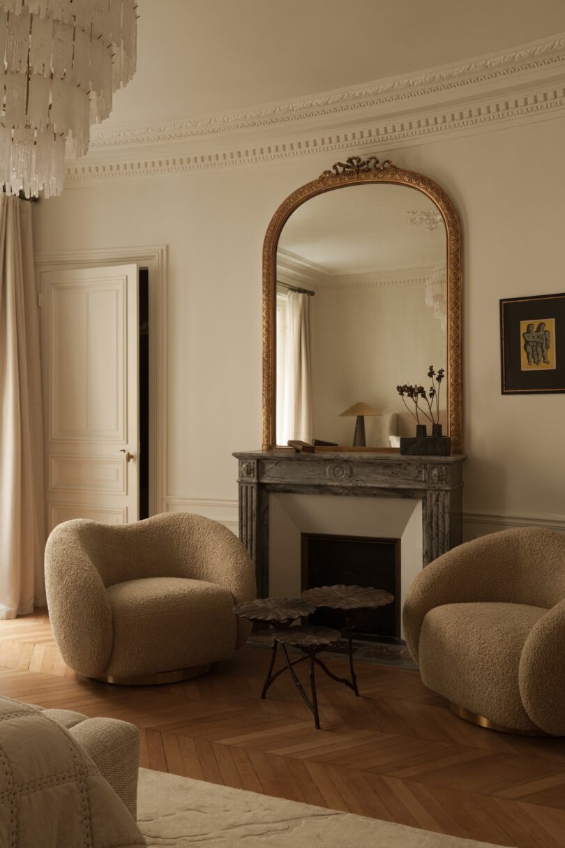 Living room corner with beige boucle armchairs, a sculptural coffee table, and herringbone parquet floors.
