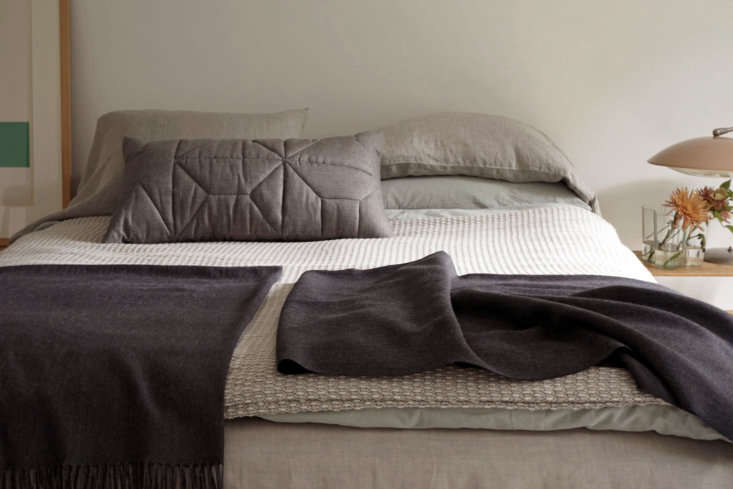 A neatly made bed with layered textiles, gray pillows, and textured blankets.