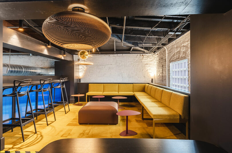 Industrial-style lounge area with yellow seating, exposed brick, and contemporary lighting.