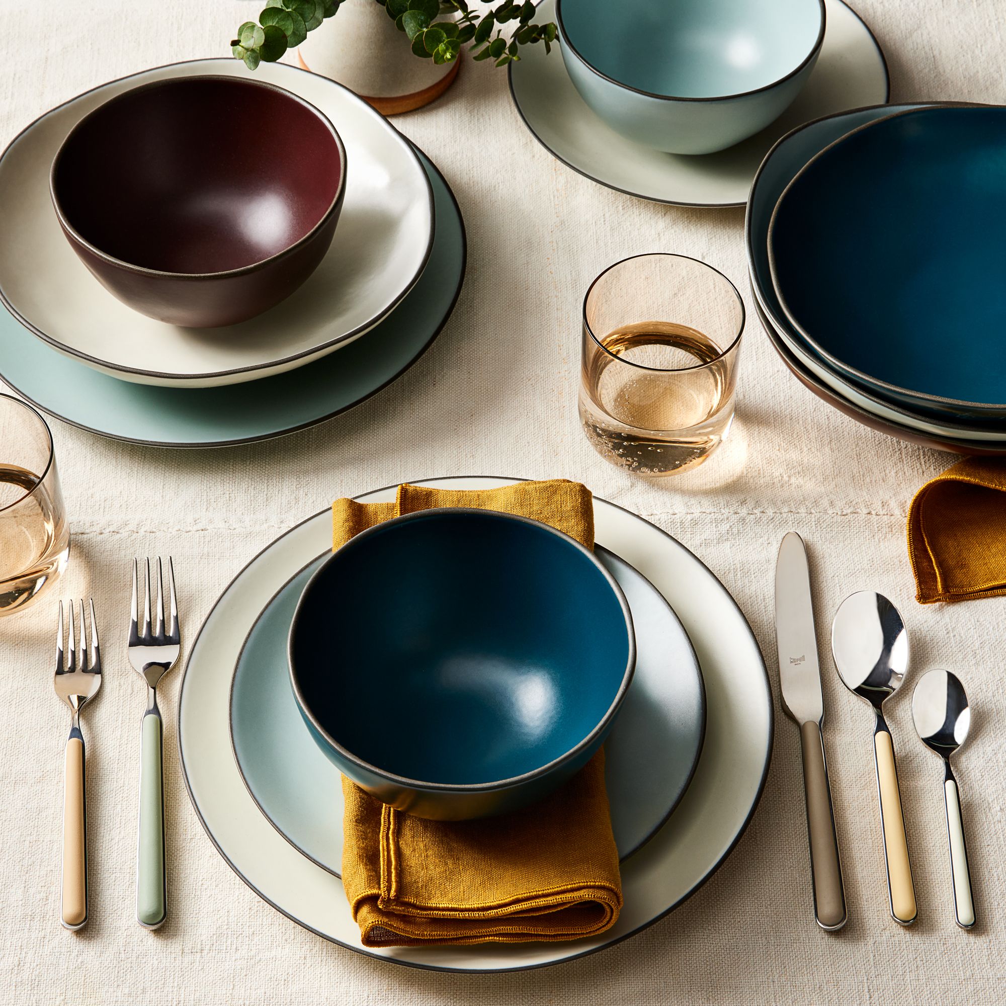 Close-up of a modern table setting with neutral-toned plates, a deep blue accent bowl, and metallic gold cutlery.