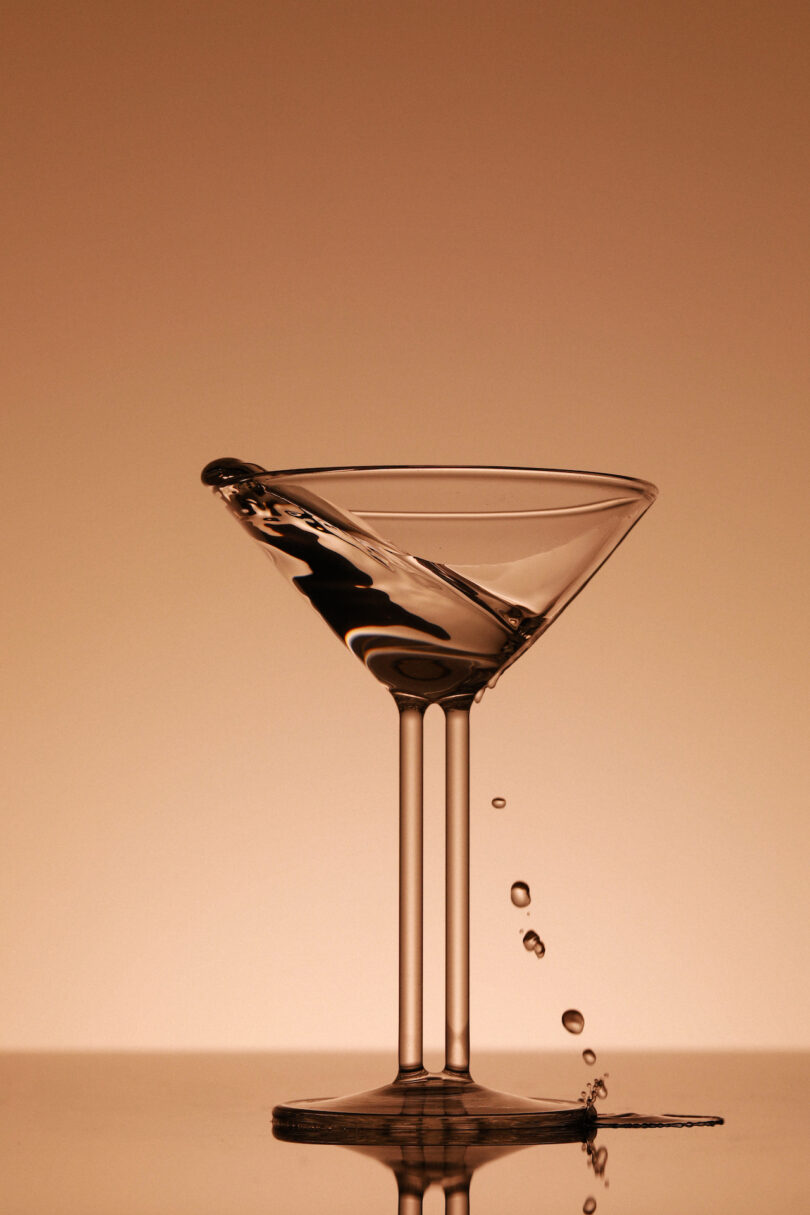 A close-up action shot of liquid splashing from a tilted martini glass against a neutral background.