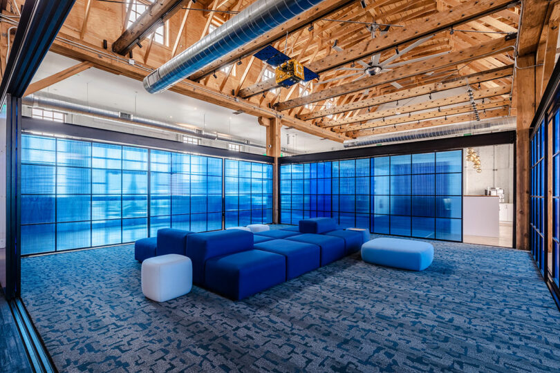 Modern office lounge with blue-tinted translucent wall panels and exposed timber ceiling beams.