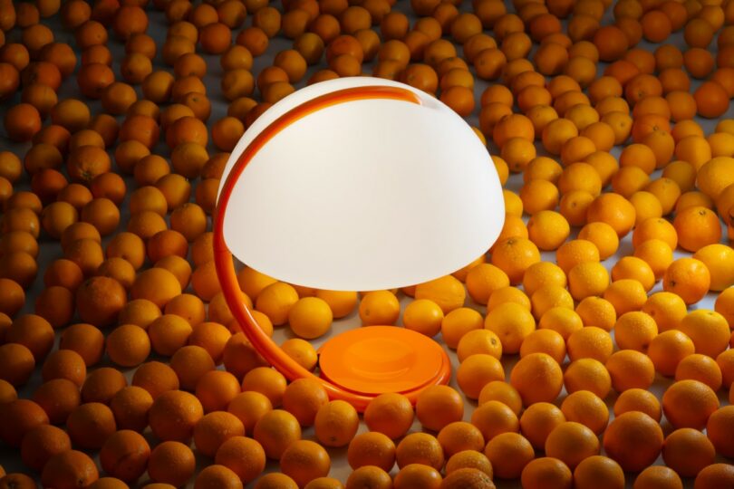 A Serpente table lamp surrounded by fresh oranges, highlighting its vibrant anniversary color.