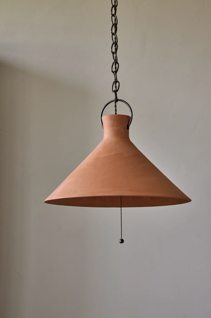 A raw, unglazed Terracotta ceramic funnel pendant light hanging by a brass loop.