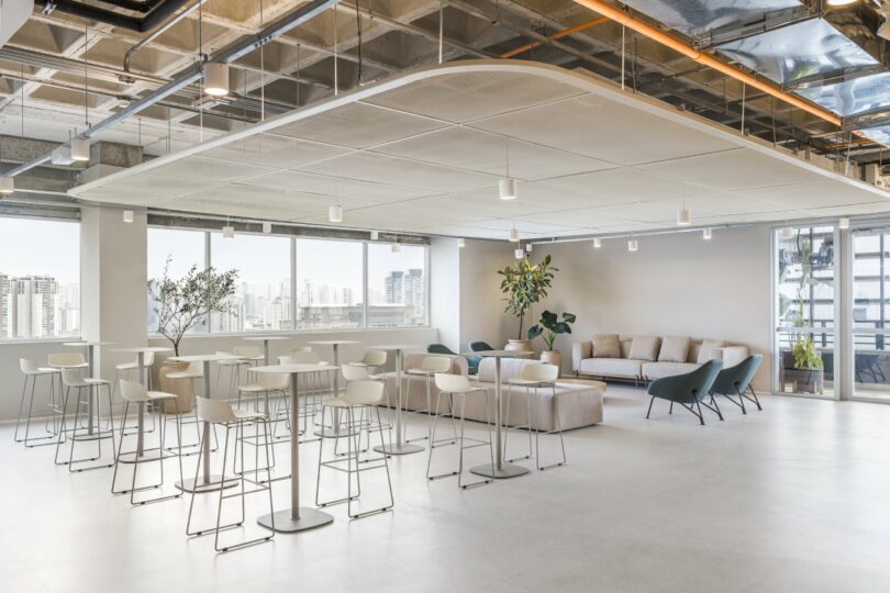 An office lounge area with bar stools and sofas overlooking the São Paulo city skyline through large windows.