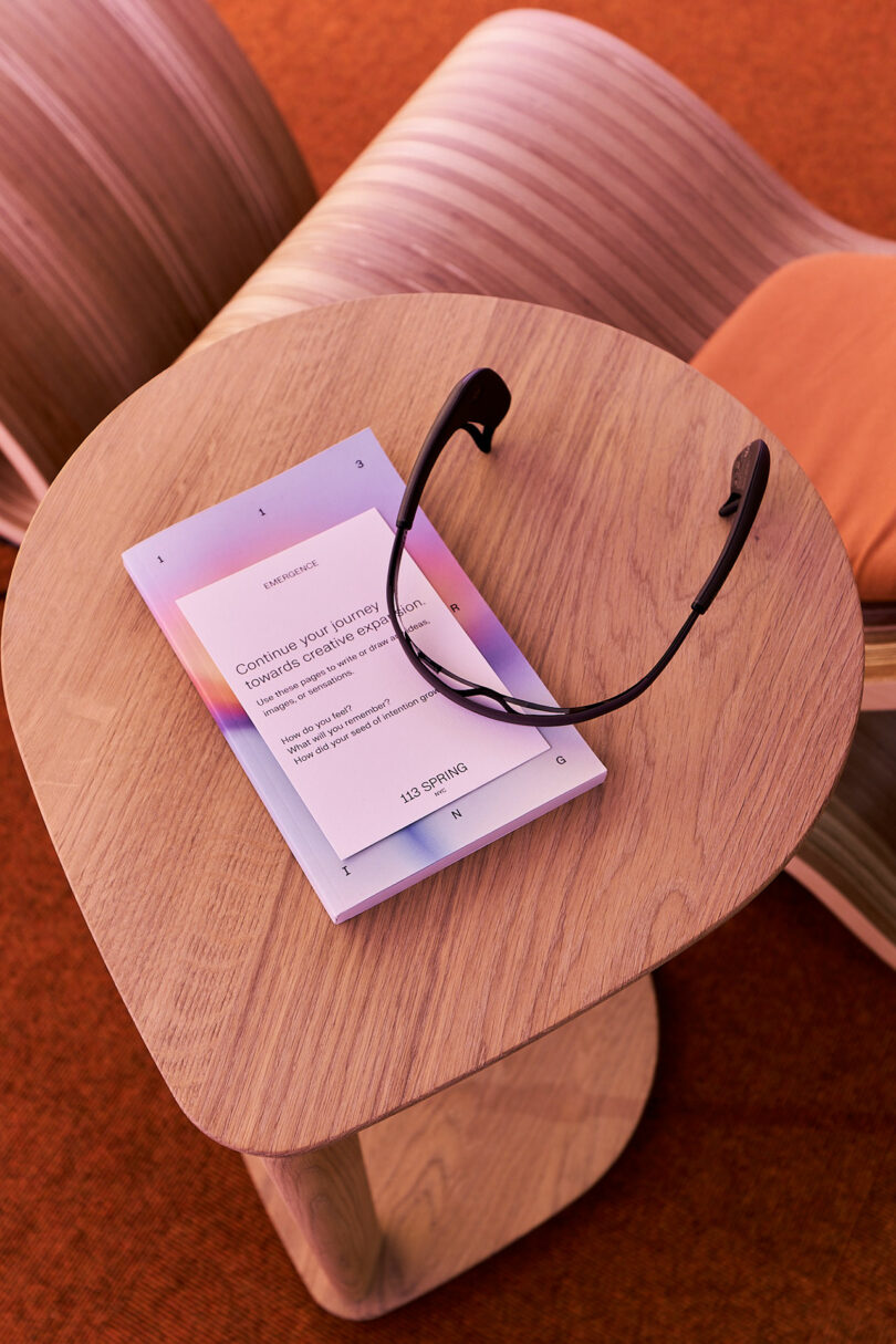 A pair of black glasses and a booklet on a wooden table next to a meditation chair.