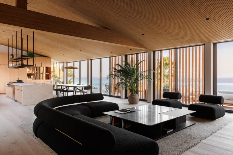 Modern open-plan living room with black sofas, floor-to-ceiling windows, and ocean views.