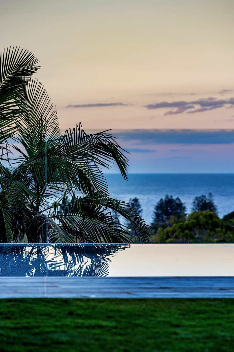 A reflecting pool flanked by palm trees overlooking the ocean at sunset.