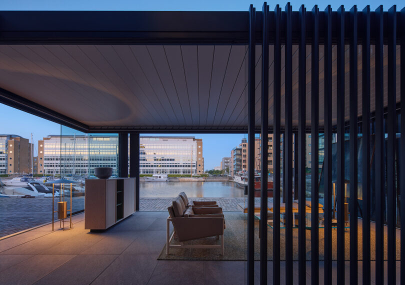 A modern waterfront lounge at dusk with minimalist furniture and ambient lighting reflecting off glass surfaces.