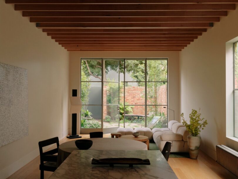 Dining area with exposed ceiling beams and large windows looking out onto a brick-walled garden.