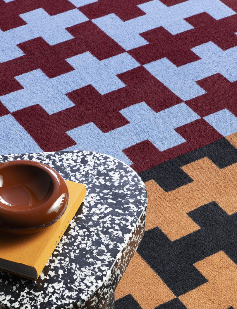 Close-up of a bold red and blue geometric rug with a speckled stone table.