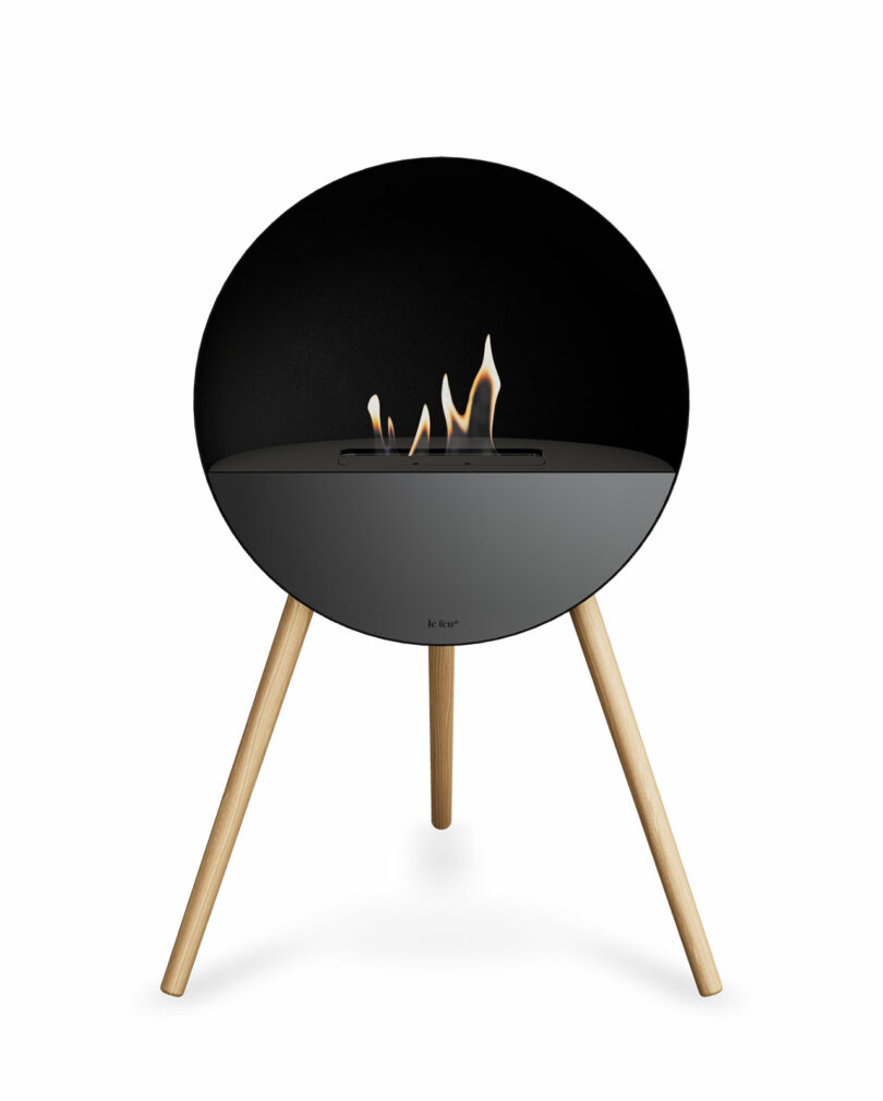 A sleek, spherical black bio-ethanol fireplace with wooden tripod legs and a flickering flame.