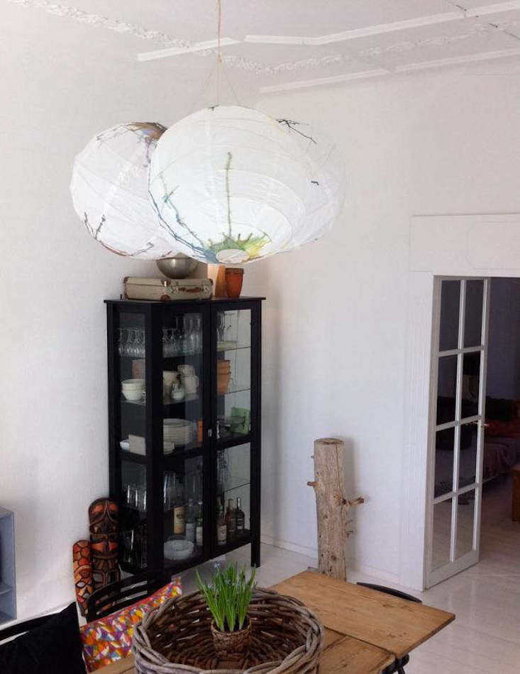 Scandinavian living space featuring watercolor-splashed paper globe lanterns above a wooden table.