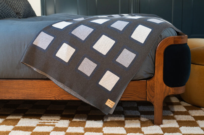 A gray and white gridded blanket draped over a modern wooden bed in a minimalist bedroom.