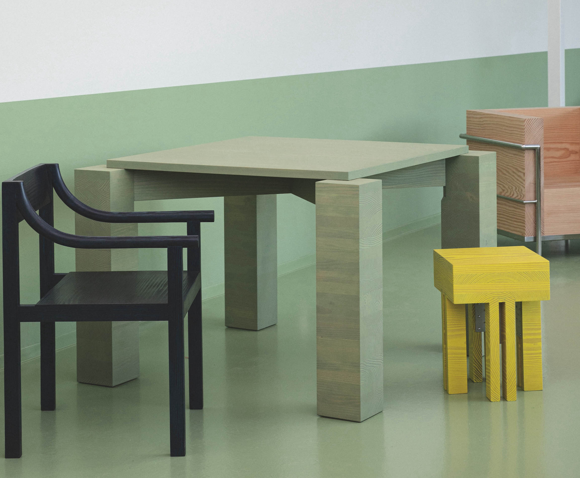 Minimalist wooden furniture including a geometric table and stools against a vibrant green and white wall.