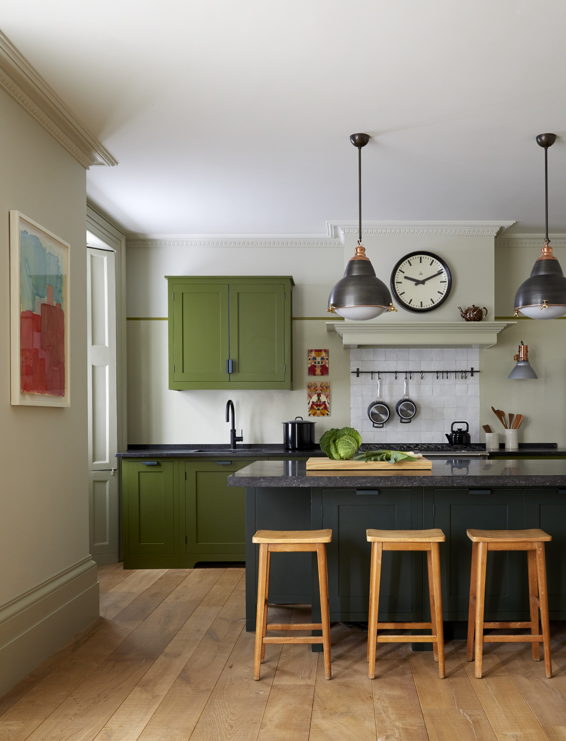 A modern kitchen with pale green walls and vivid olive green cabinetry overlooking a garden.