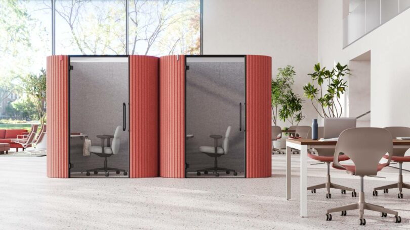 Two red acoustic pods in an office space, each containing a full-sized ergonomic desk chair.
