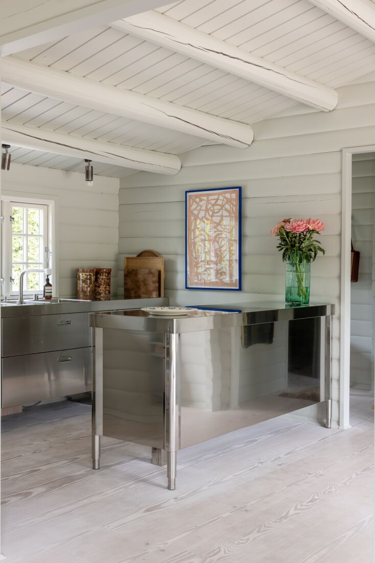 A shiny Alpes Inox stainless steel kitchen set against a Scandinavian cabin interior.