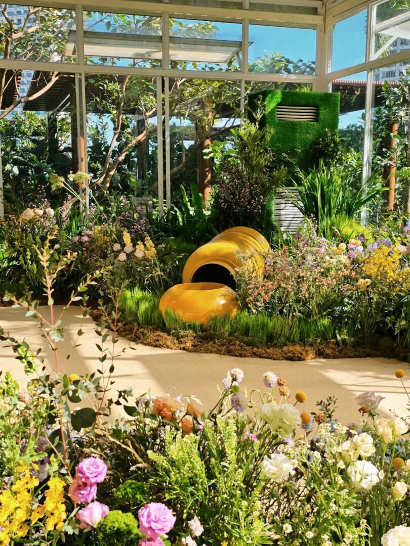 A sunlit indoor garden space with modern sculptural elements and vibrant flowers.