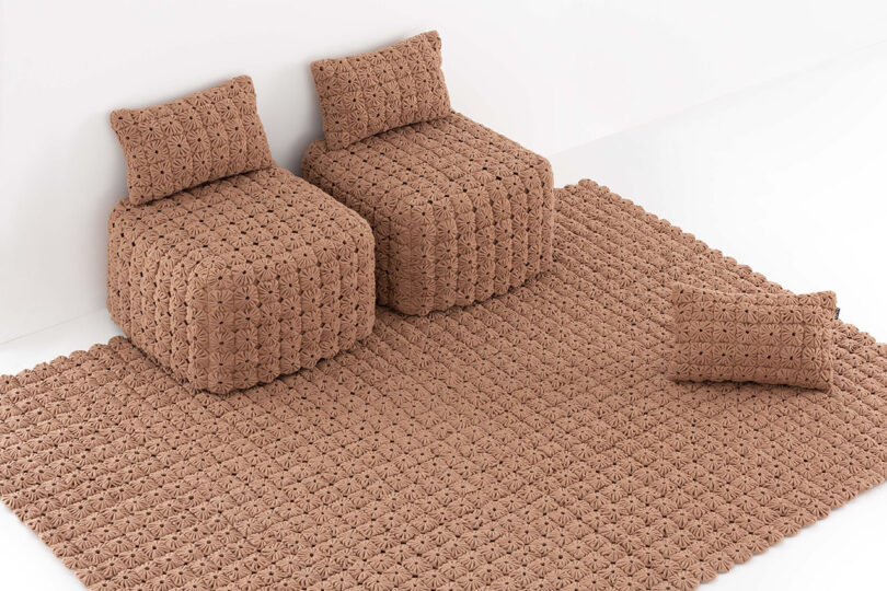 Two textured brown armchairs and a rectangular rug with a crocheted pattern in a minimalist setting.