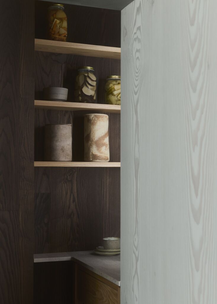 Interior of a kitchen pantry featuring dark oiled ash wood, shelves with ceramics, and pickled vegetables.