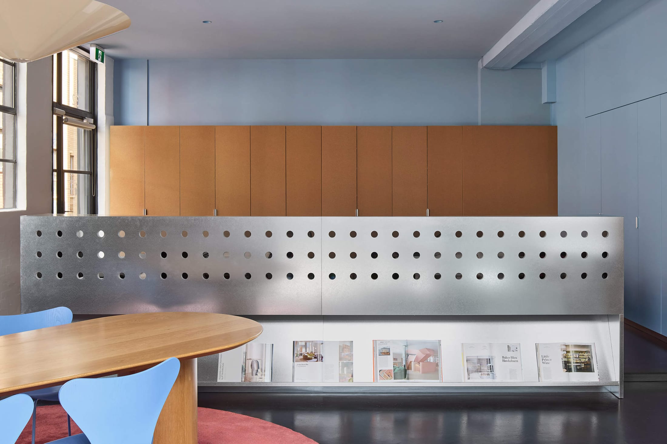 Modern open-plan studio featuring perforated metal partitions and minimalist wooden furniture with blue accents.