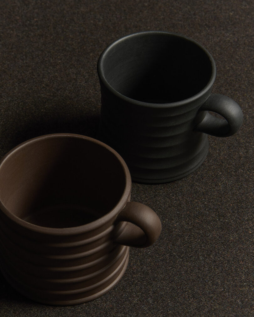 Side-by-side view of black and brown ribbed ceramic mugs.